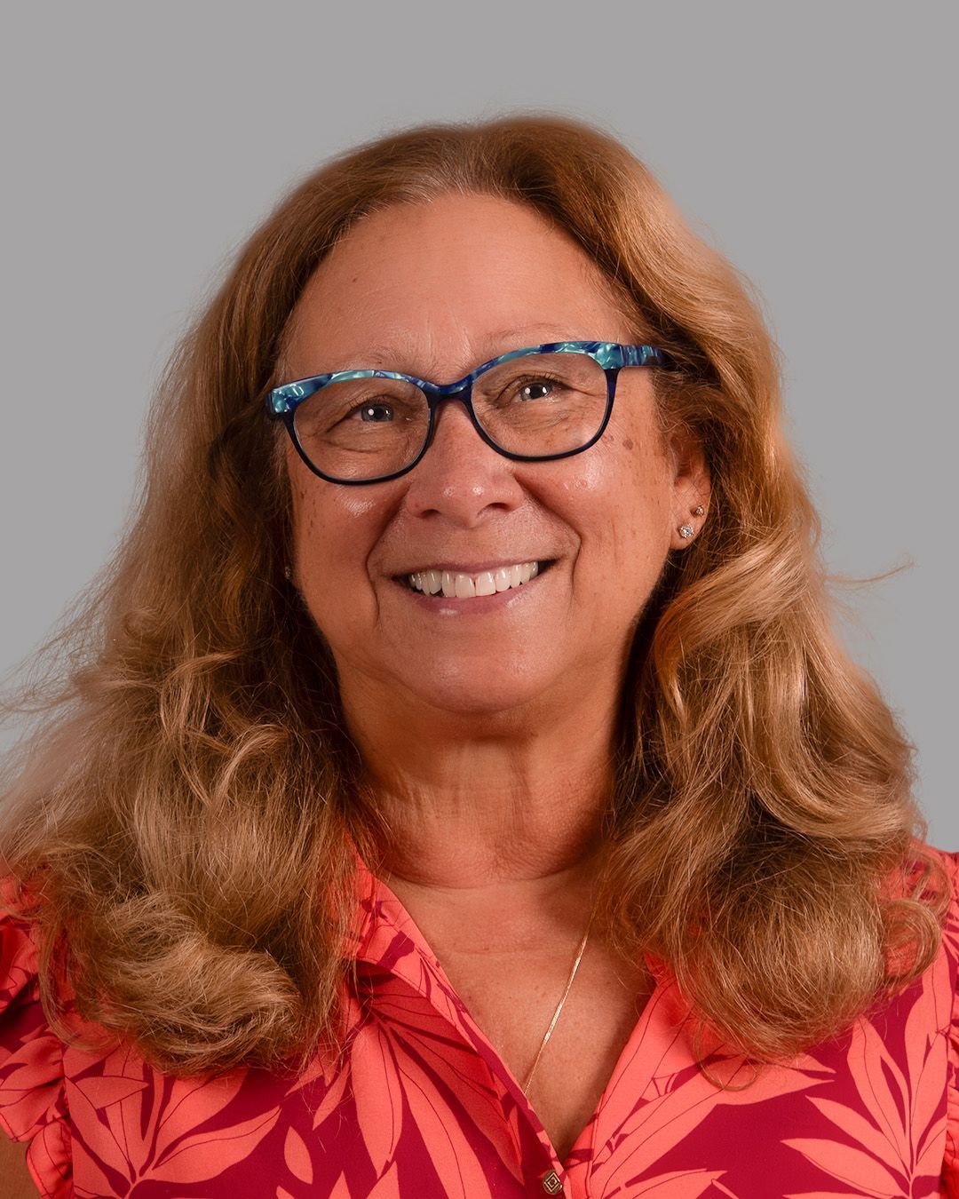 A woman wearing glasses and a red sweater is standing in front of a brick wall.