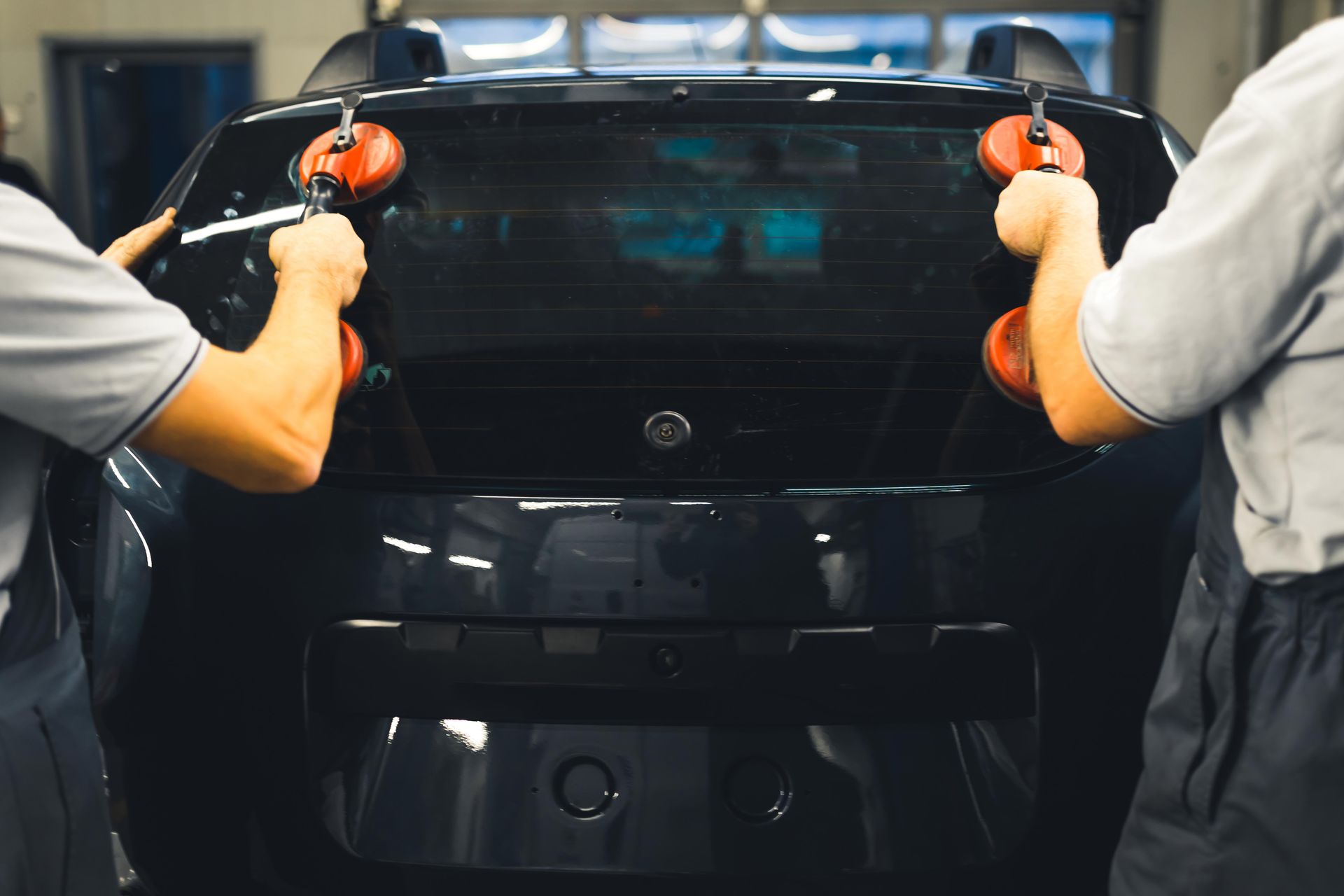 Auto glass technicians installing replacement windshield on car at repair shop.