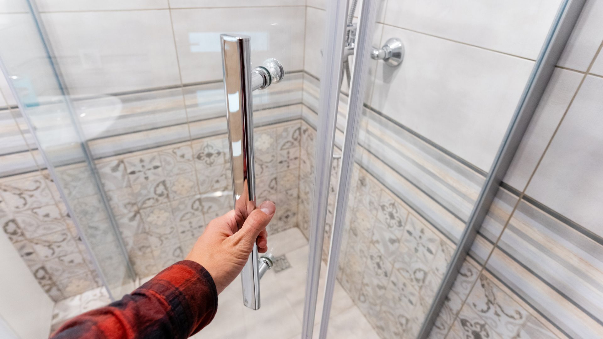 A person is opening a glass shower door in a bathroom. A person is opening a glass shower door in a bathroom.
