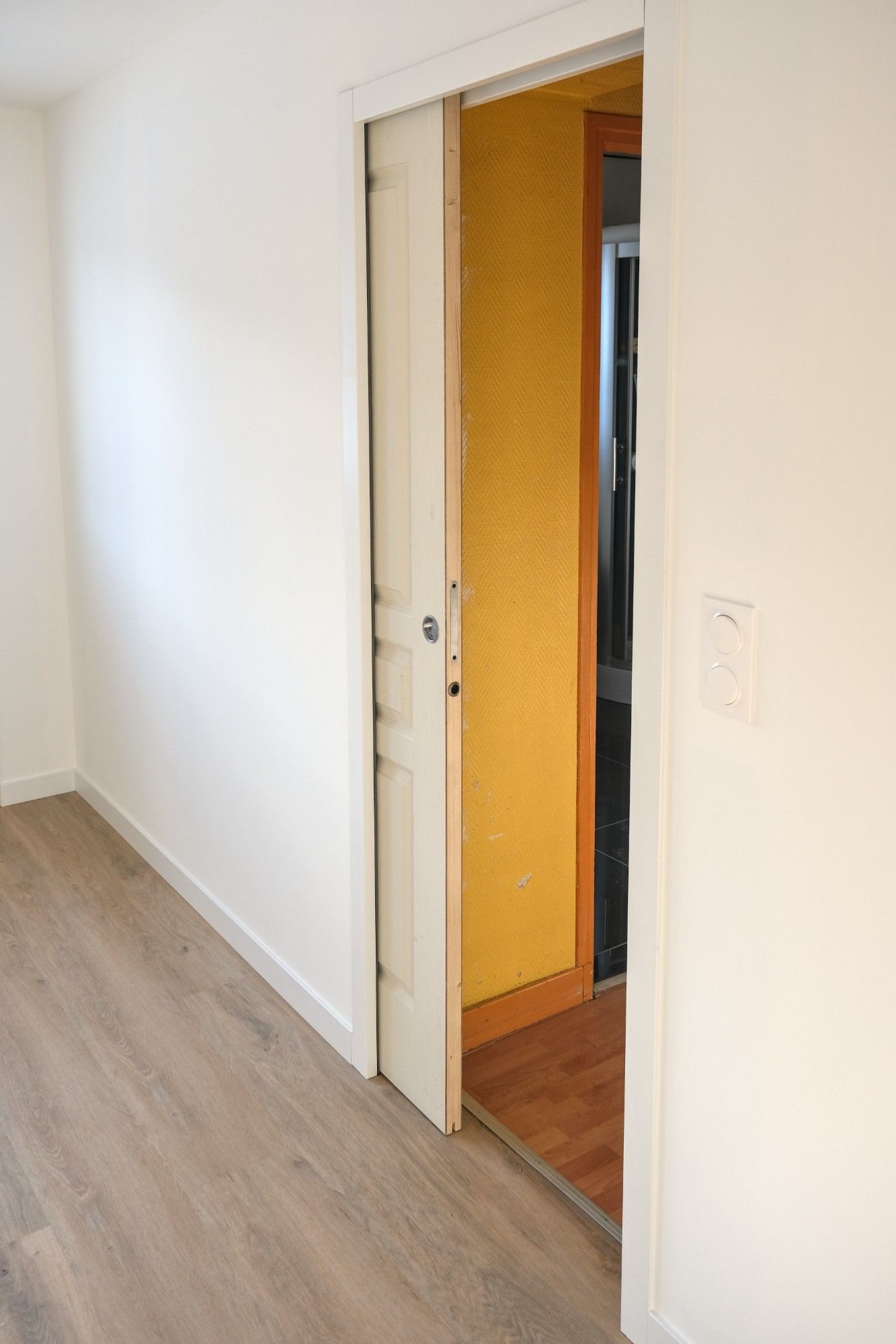 A hallway with a sliding door leading to a kitchen.