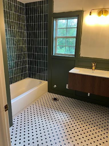 A bathroom with a tub, sink, mirror and window.