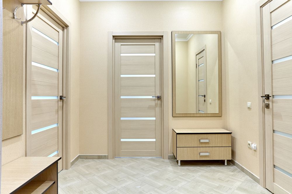 A hallway with wooden doors, a mirror and a dresser.