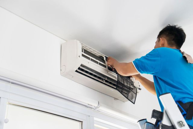 Technician cleaning a wall-mounted air conditioner on a ladder