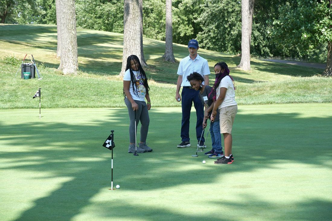 A group of four people practicing putting on a sunlit golf green.