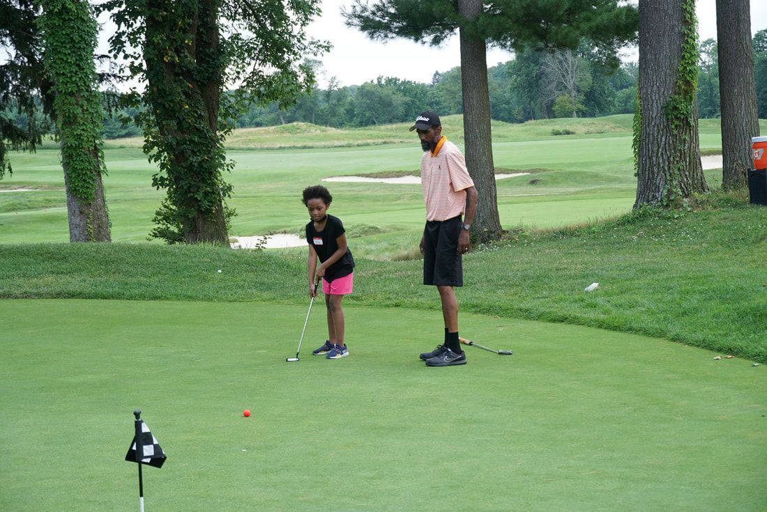 A person teaches a child how to putt on a grassy golf green.