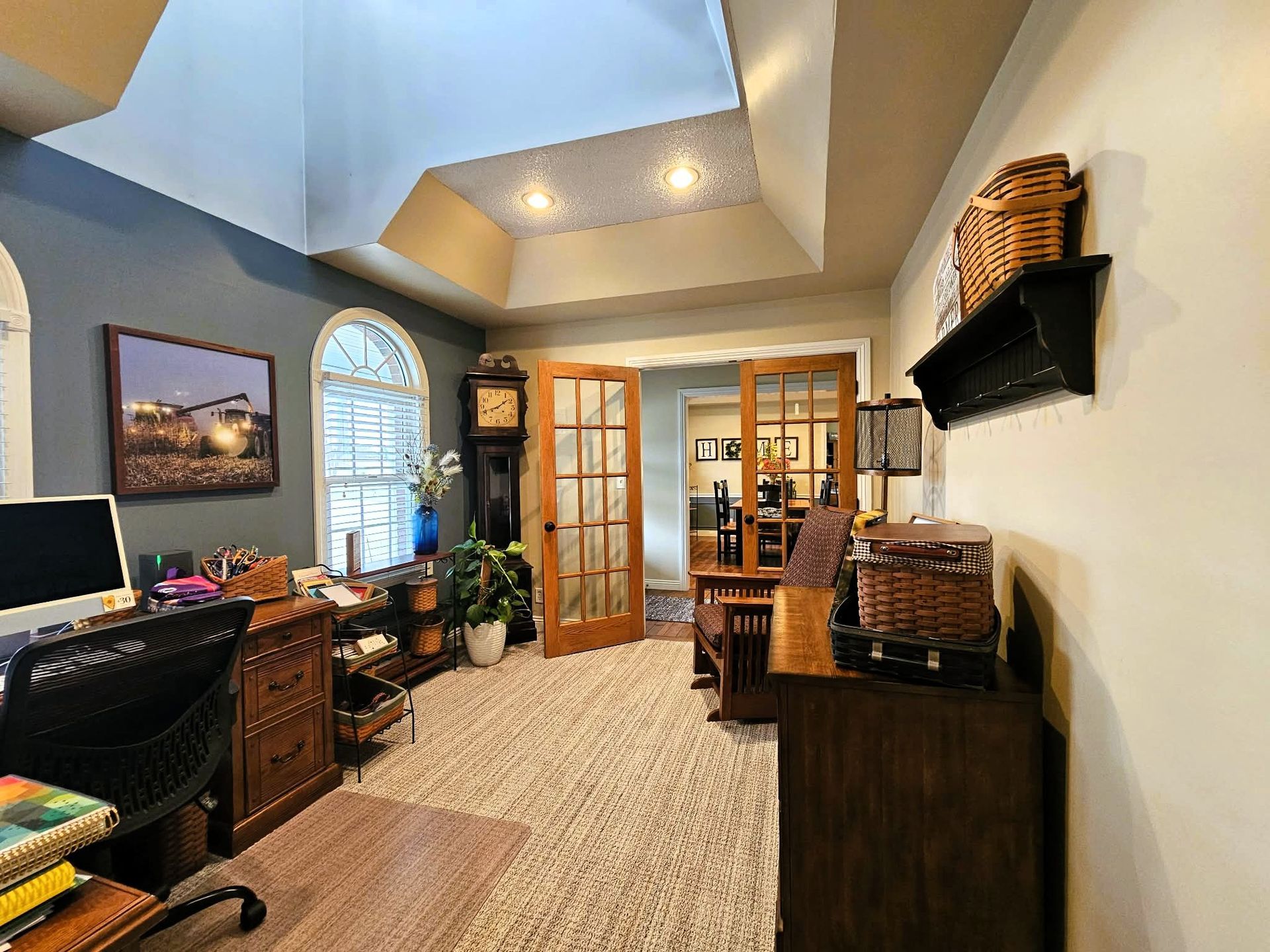 Home office with vaulted ceiling, desk, computer, bookshelves, and French doors leading to another room