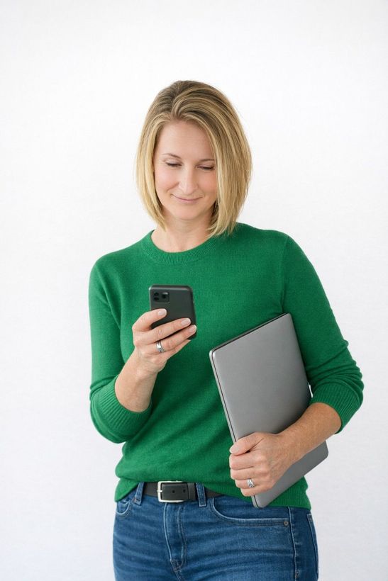 A woman is sitting at a desk with a laptop and a vase of flowers.