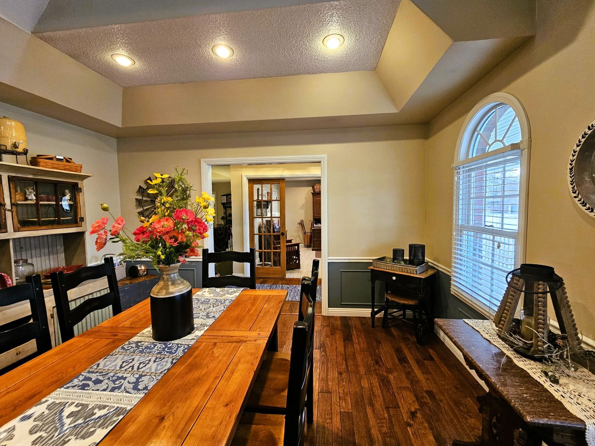 Dining room with long wooden table, black chairs, floral centerpiece, and bright windowed wall