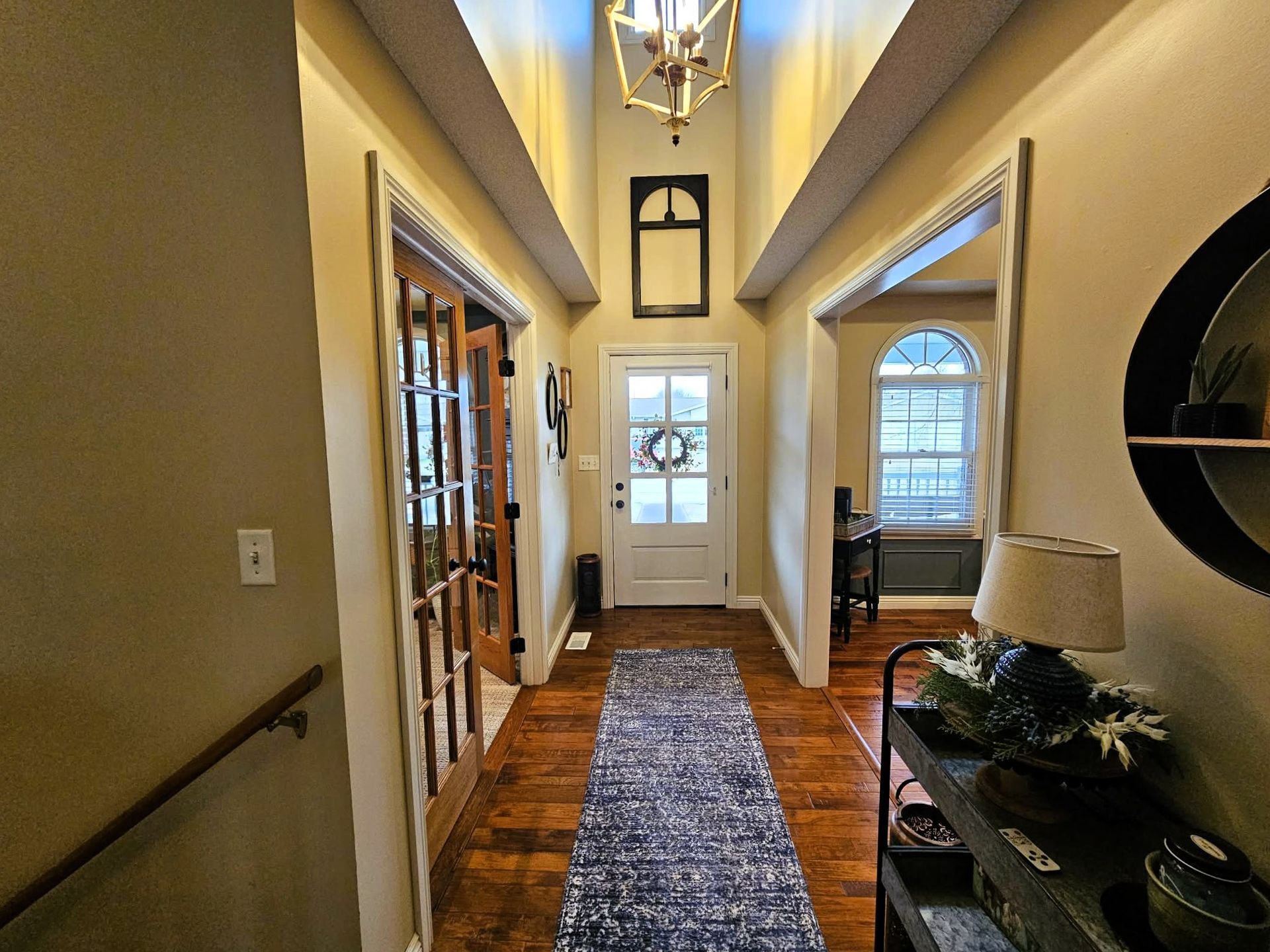 Narrow hallway with vaulted ceiling, hardwood floors, runner rug, and a door at the end.