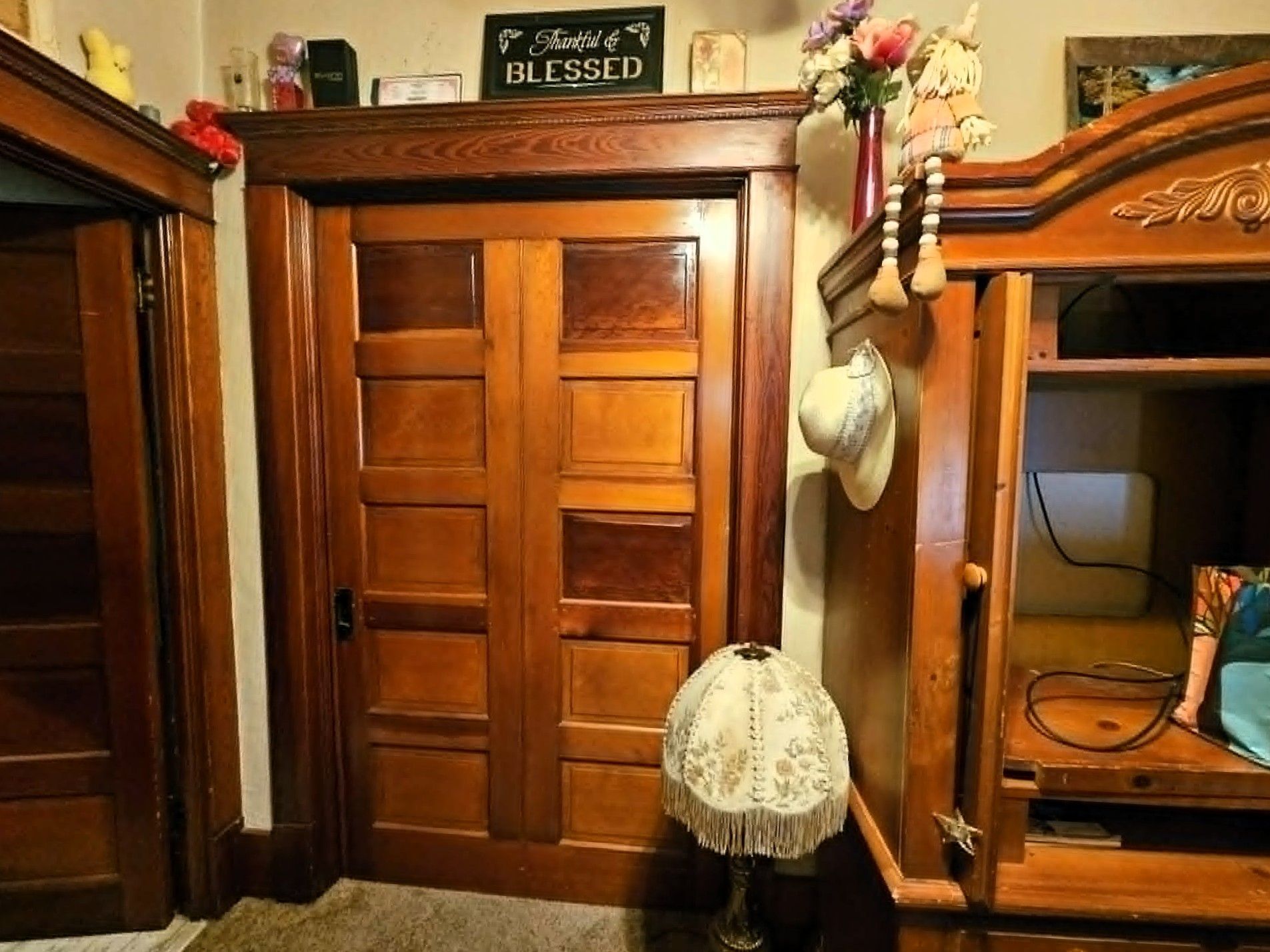 Wooden doors between a bookcase and mirror, with hanging decorative items in a cozy room.