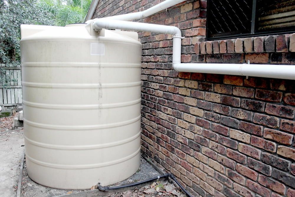A Large White Water Tank Is Sitting Next To A Brick Wall — DMK Plumbing in South West Rocks, NSW