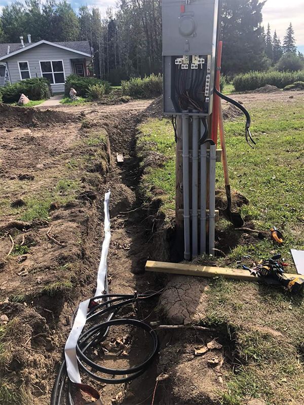 Trench with electrical conduit and wiring near a gray electrical meter box, beside a house on grass.