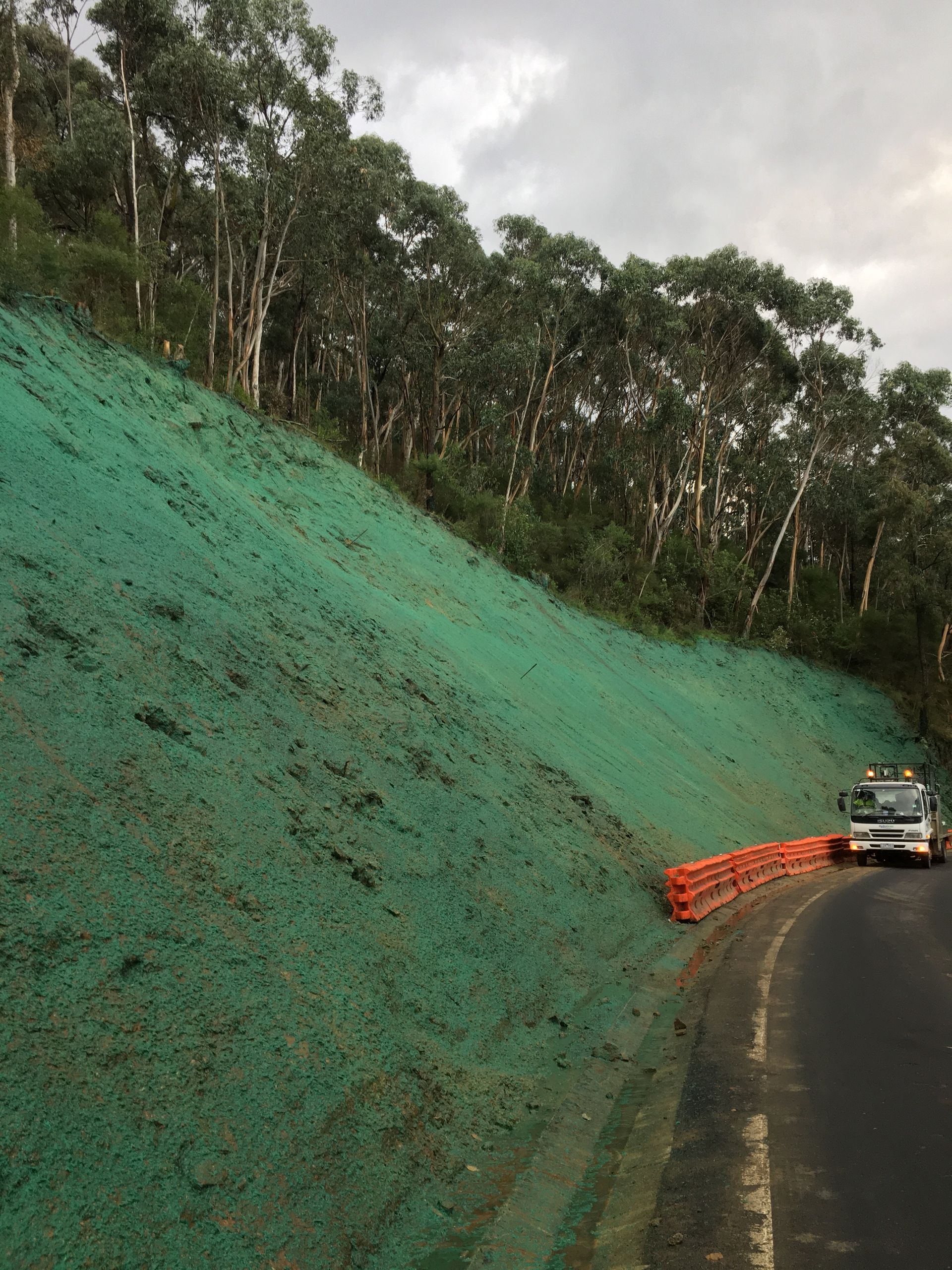 A truck is driving down a road next to a grassy hill