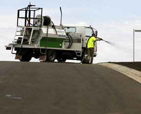 A man in a yellow vest sprays water from a truck