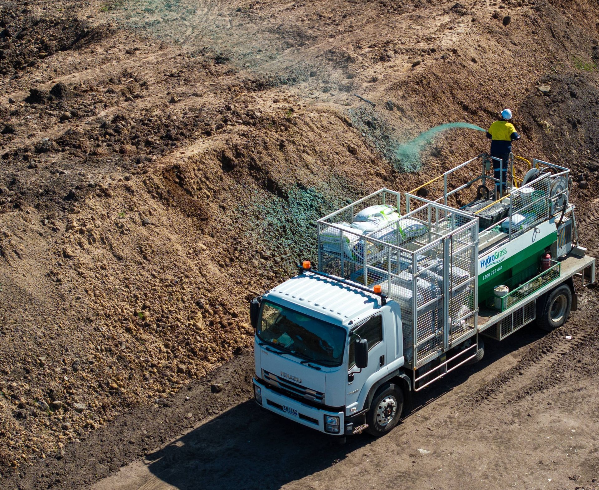 A white truck with a green tank on the back is driving through a dirt field