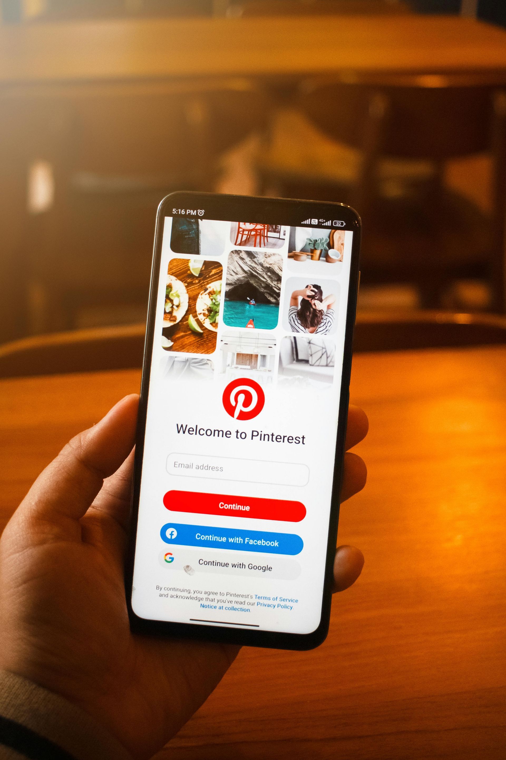 Hand holding a smartphone showing the Pinterest app on a warm-lit table background