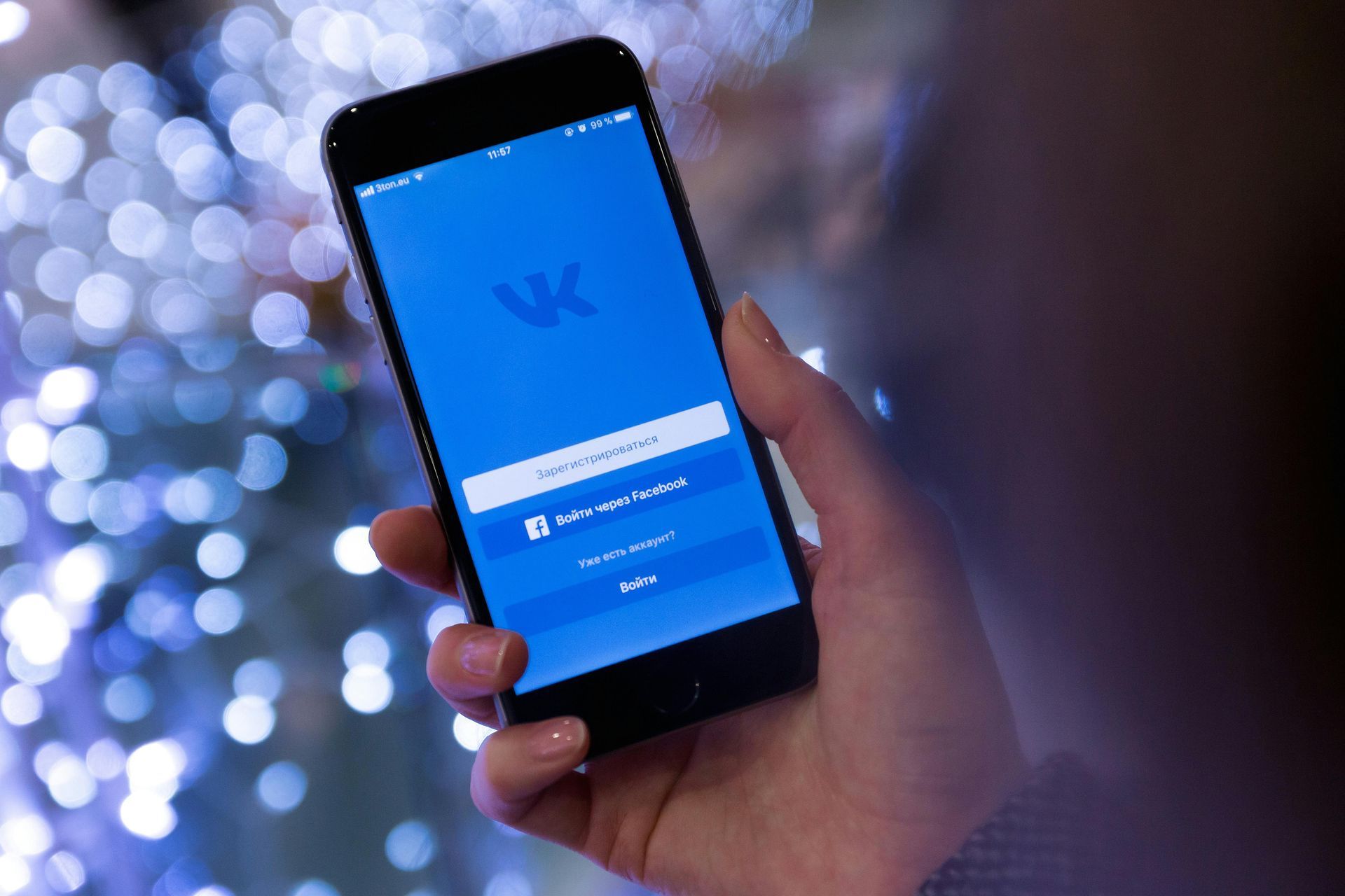 Hand holding a smartphone showing the VK login screen on a blue display