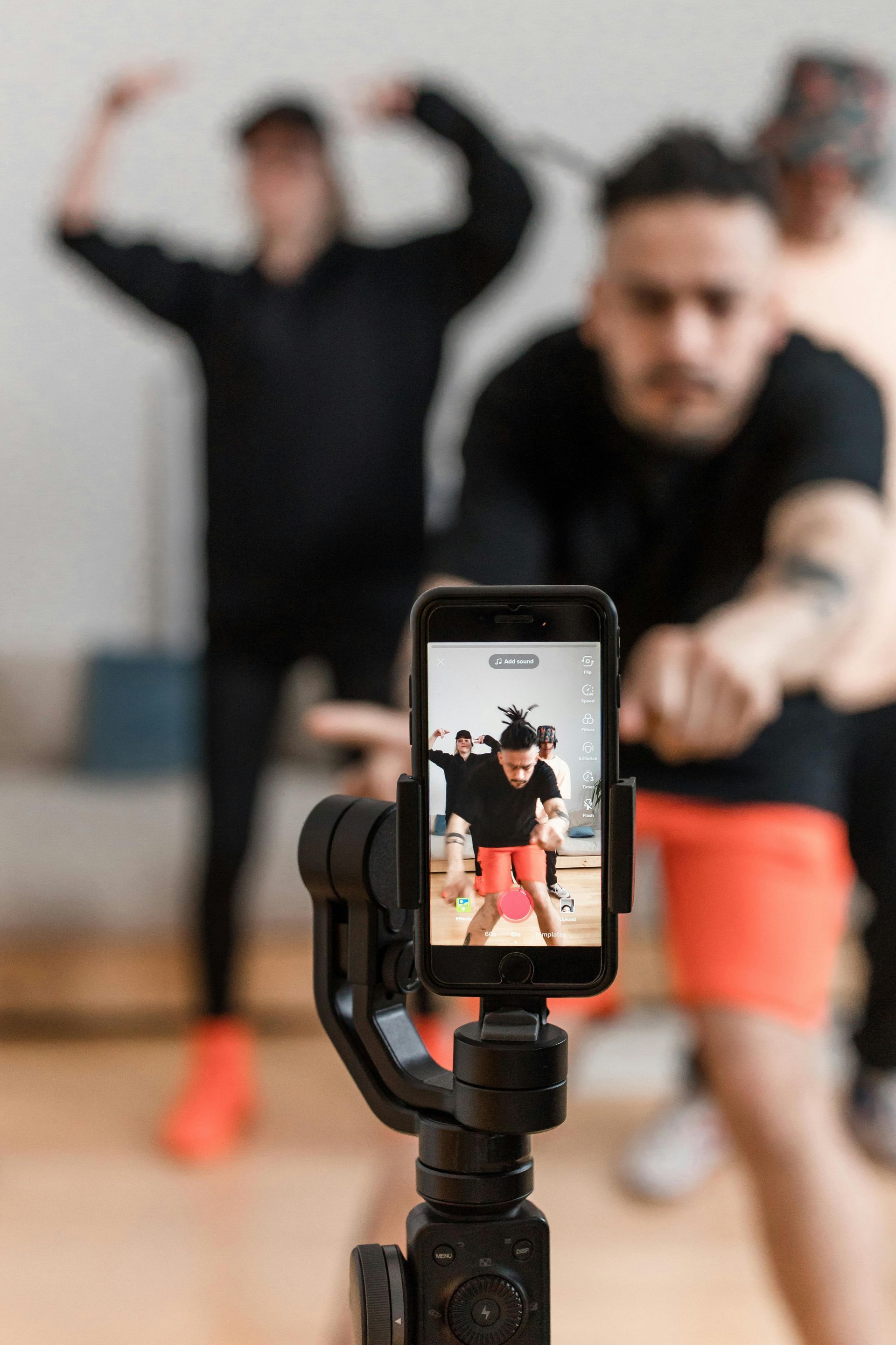 Phone on tripod records people exercising in a gym, with one person in focus and others blurred behind.