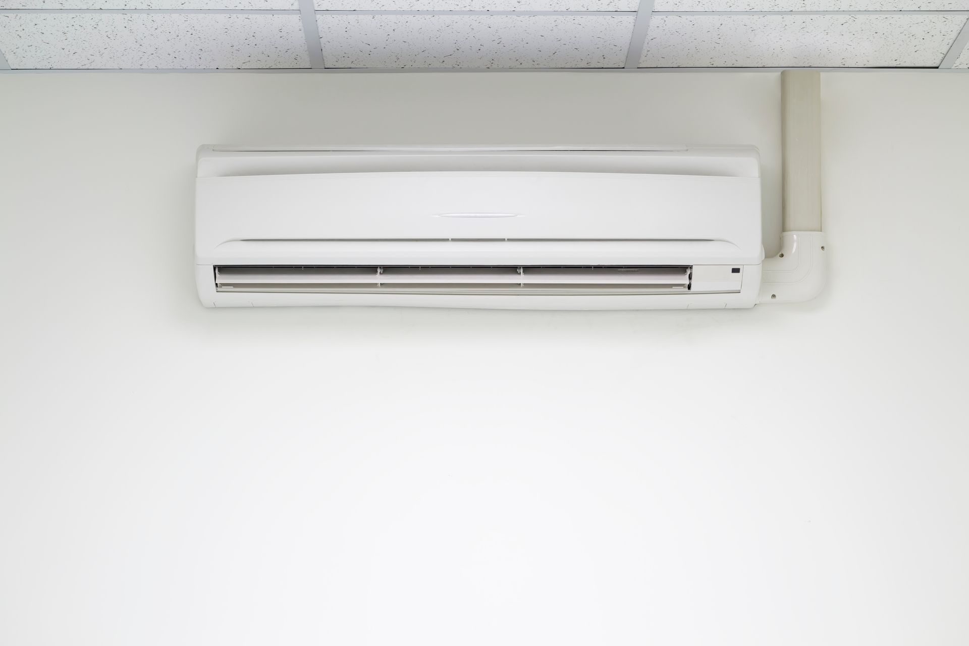 Row of white air conditioning units mounted on a building's exterior wall.