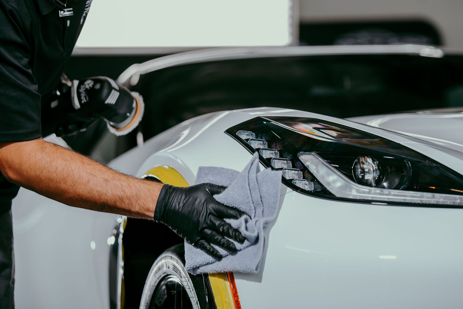 A man is polishing the headlight of a white car.
