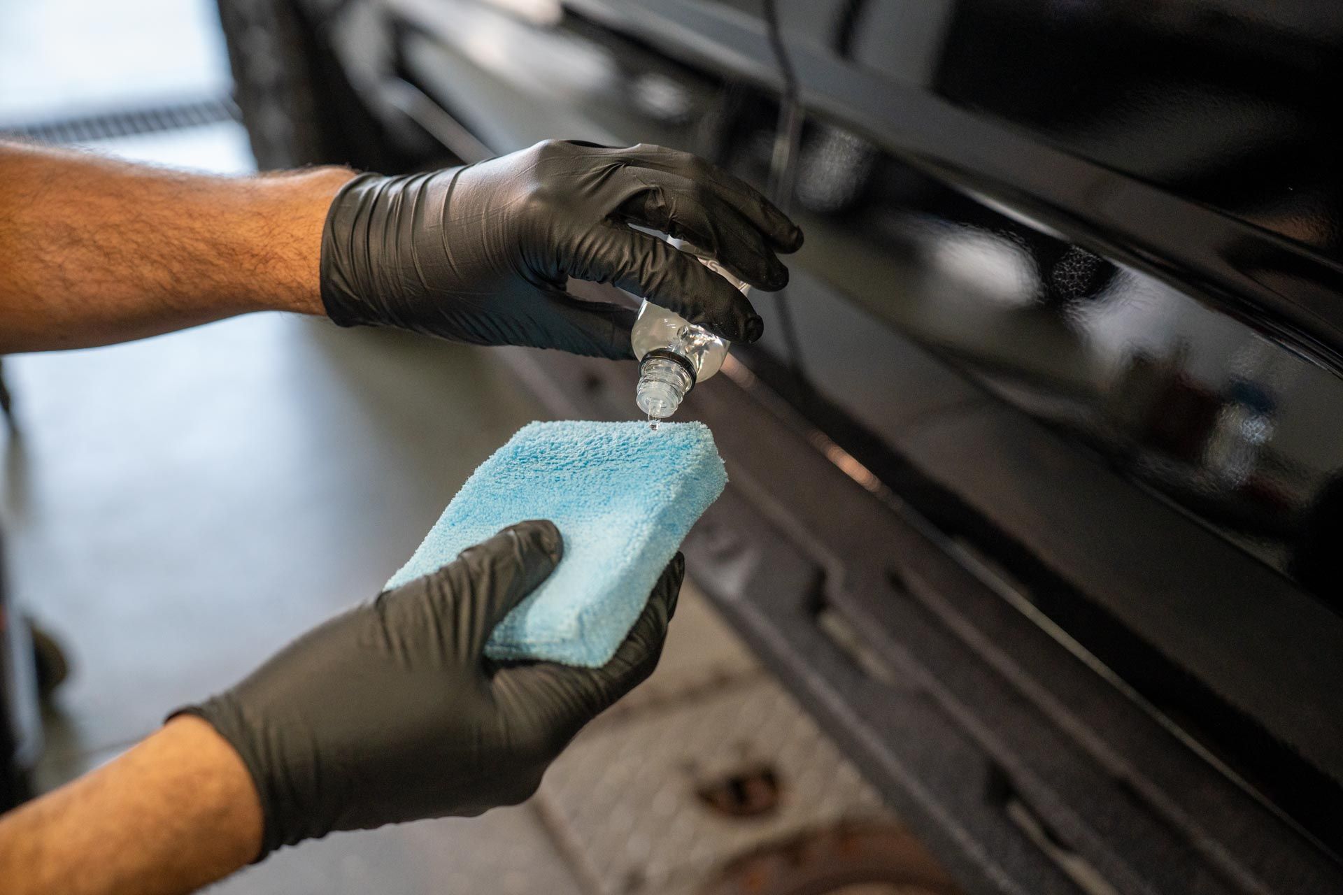 Person wearing black gloves applying product to car with a blue sponge.