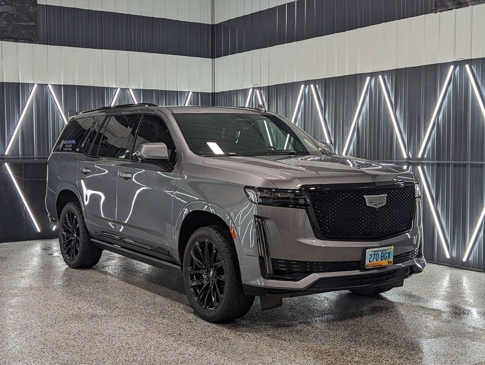 A gray cadillac escalade is parked in a garage.