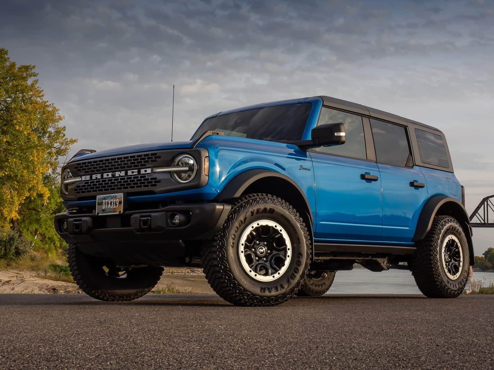 A blue ford bronco is parked on the side of the road next to a body of water.