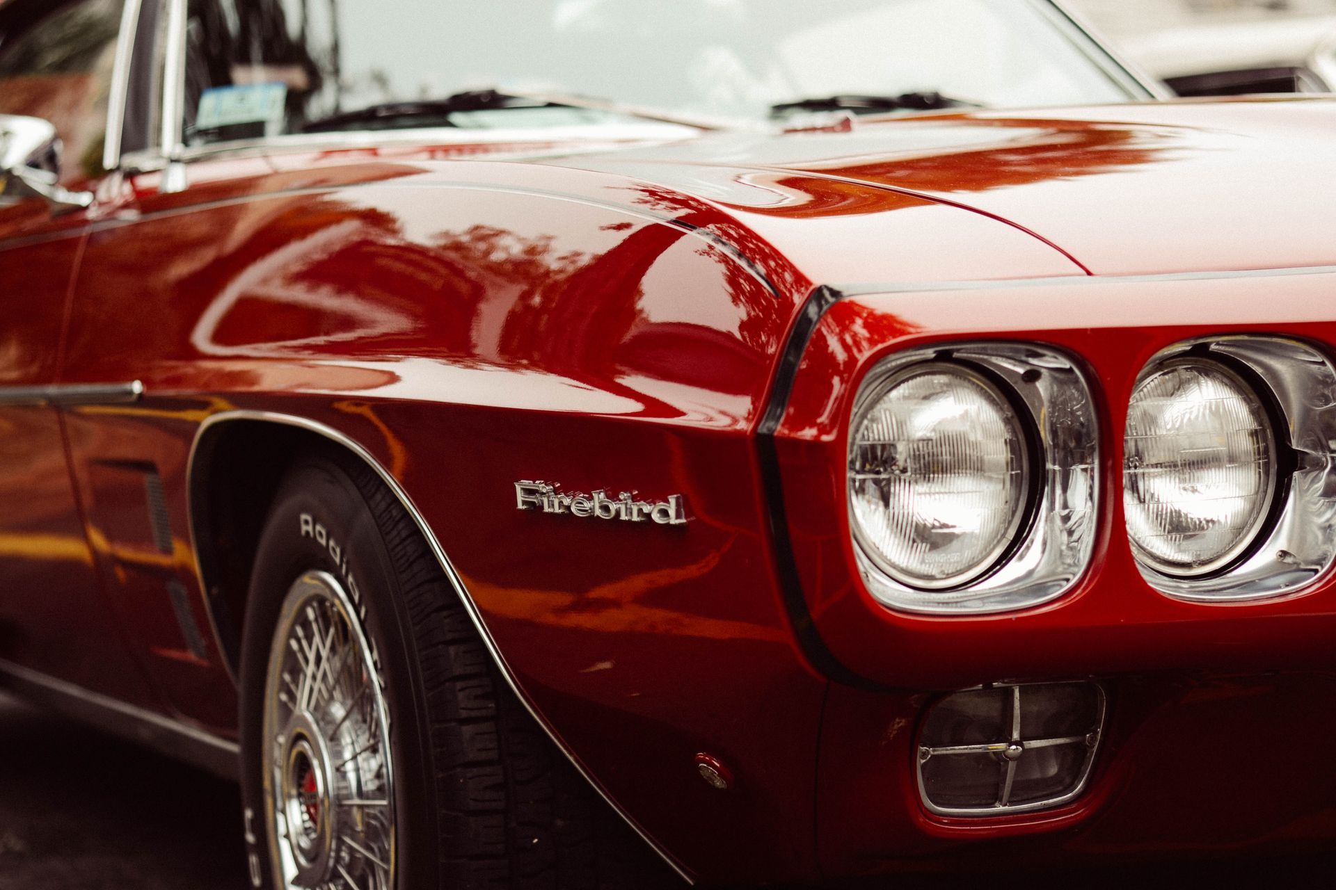 Red vintage Pontiac Firebird car with shiny chrome headlights.