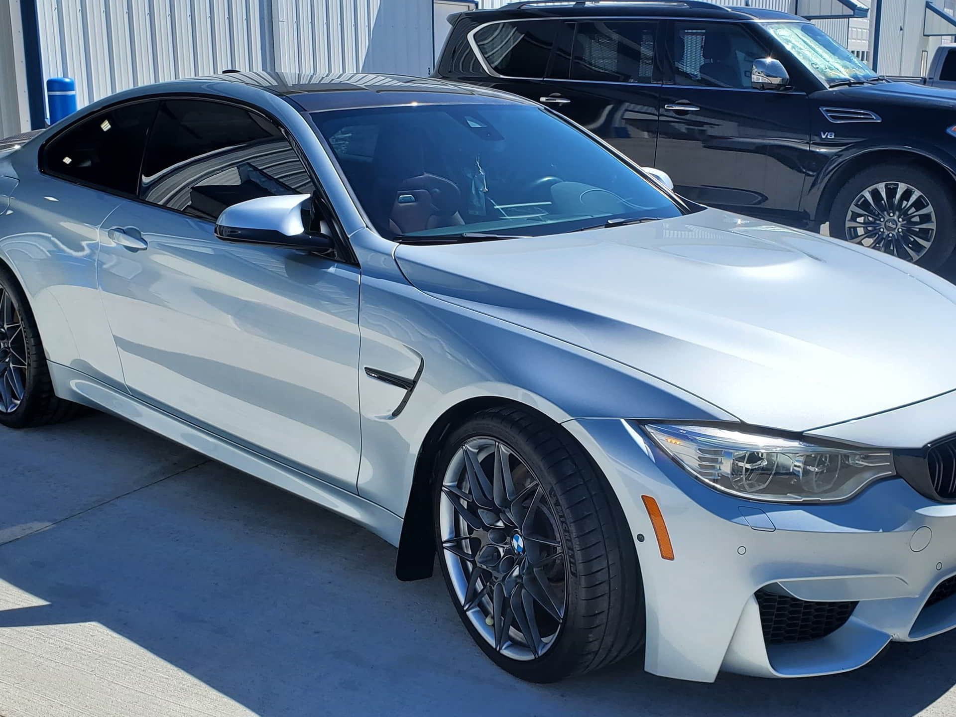 A silver bmw m4 coupe is parked next to a black suv.