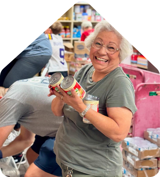 Smiling woman holding a canned food item at a food pantry donation table