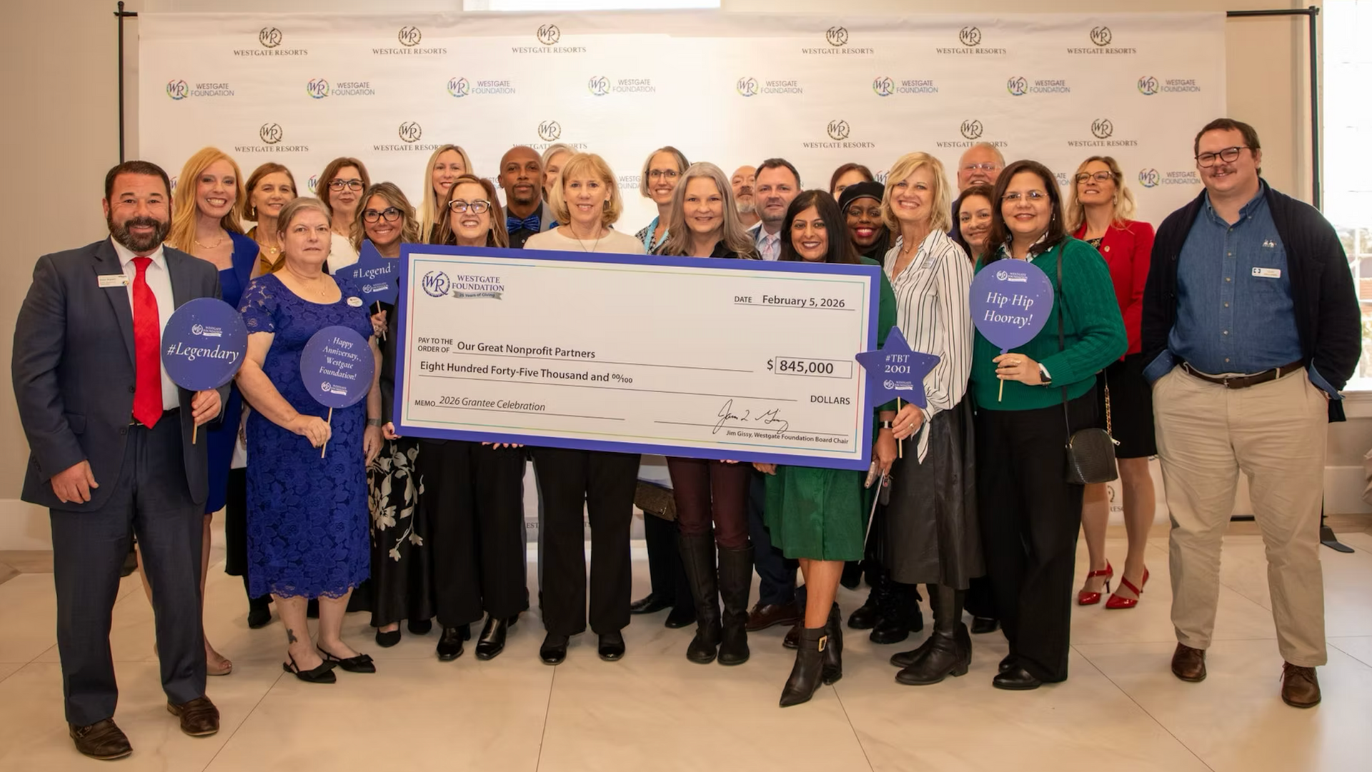 Group of people holding an oversized check at a celebratory indoor event.