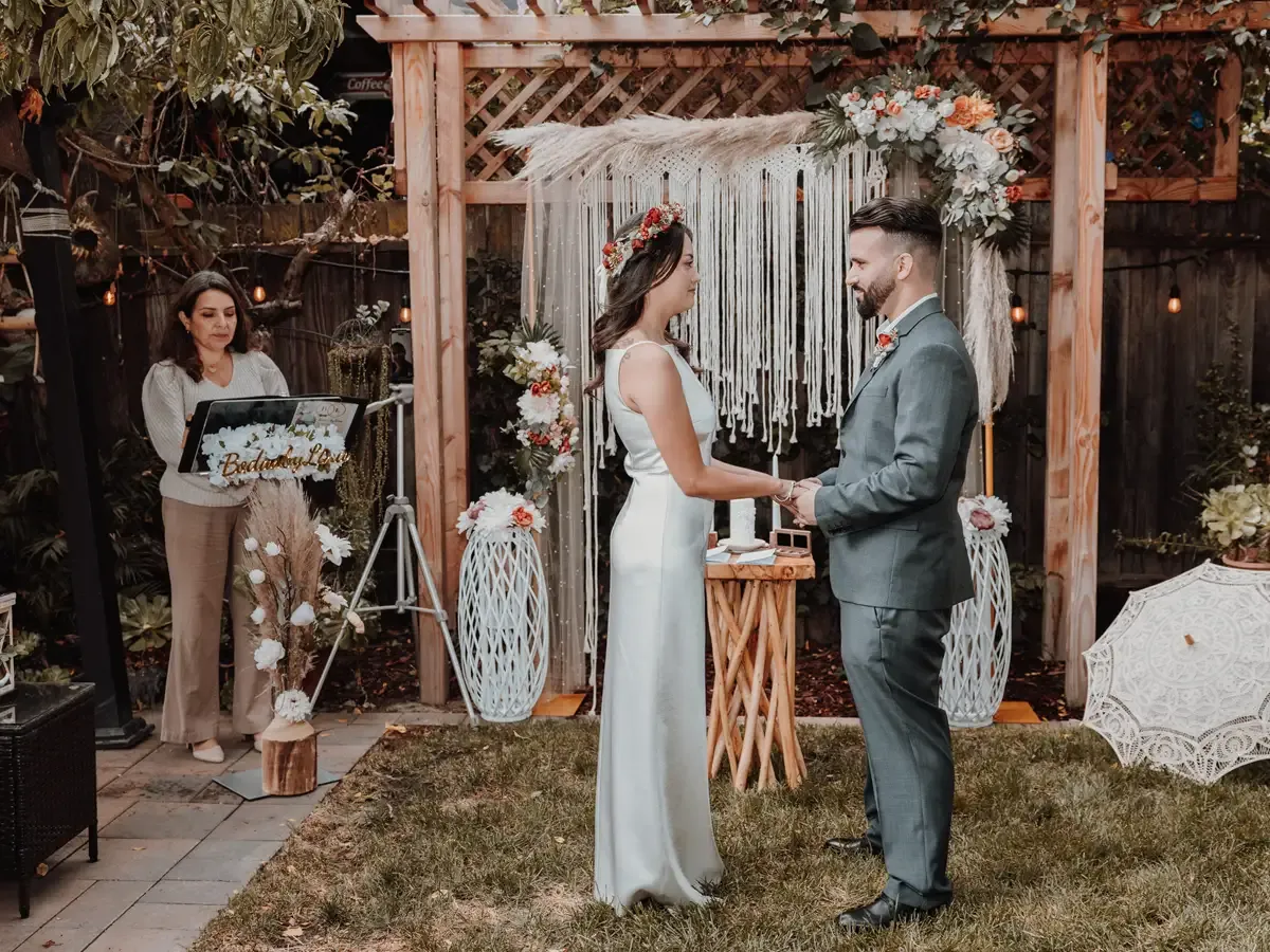 Wedding ceremony: couple holding hands under wooden arch decorated with flowers, Bodas by Lina, Santa Clara, CA.
