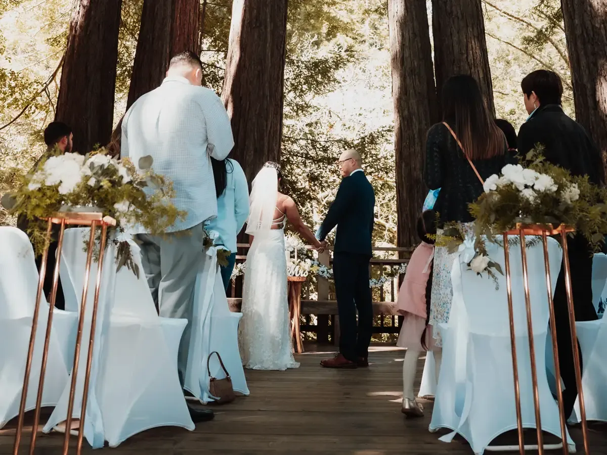 Wedding ceremony outdoors, bride and groom hold hands on a wooden platform. Bodas by Lina, Santa Clara, CA.
