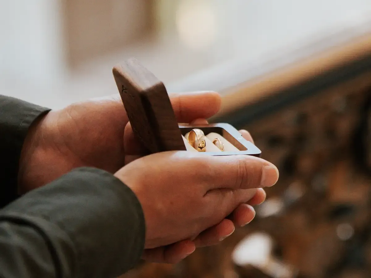 Hands holding an open wooden ring box, containing two gold rings. Bodas by Lina, Santa Clara, CA.