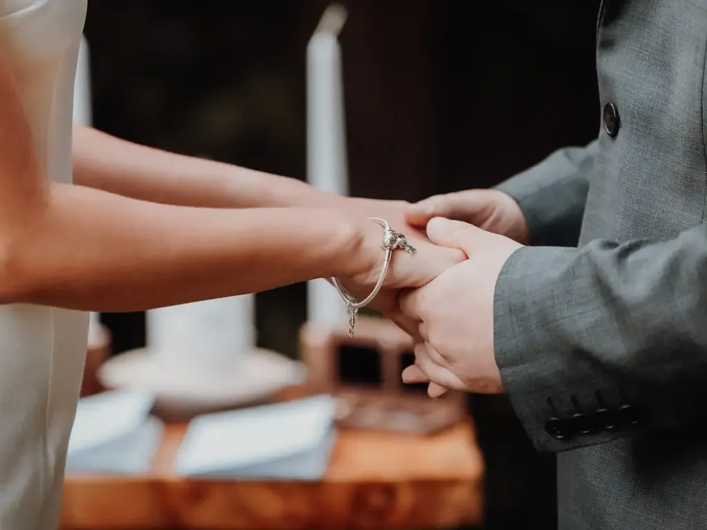 Couple holding hands during a wedding ceremony, with candles and a wooden table. Bodas by Lina, Santa Clara, CA.