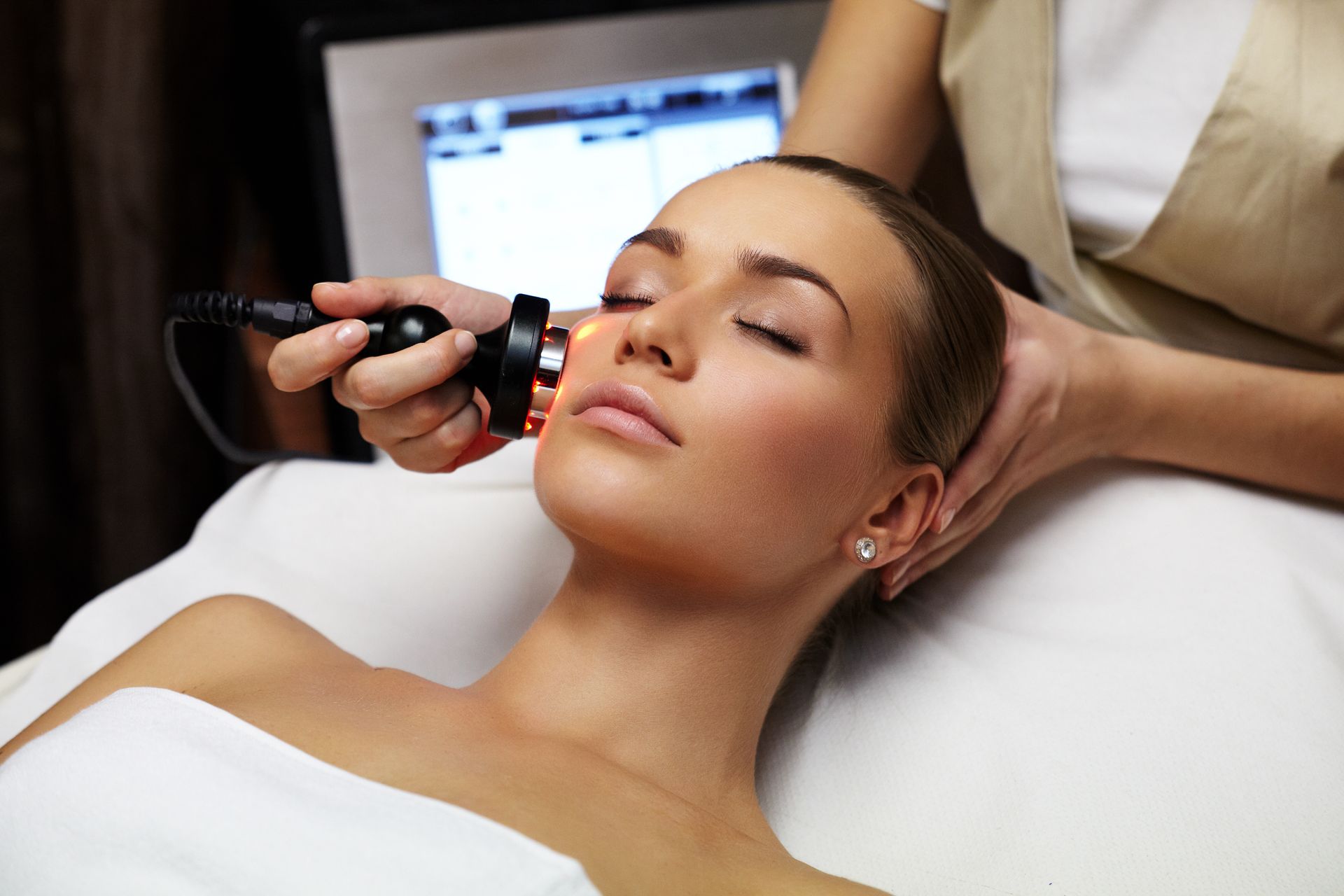 A woman receiving a non-invasive laser facial treatment on her cheek at a beauty spa clinic