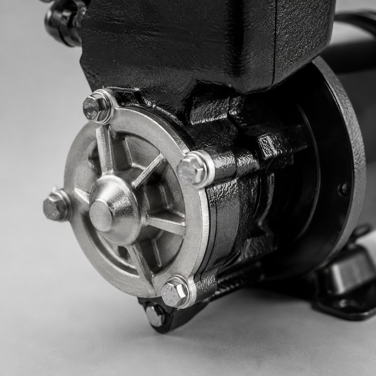 Close-up of a black mechanical pump housing with a silver bolted cover on a gray background