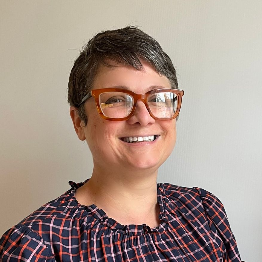 Woman with short gray hair, glasses, and a patterned top smiles at the camera.