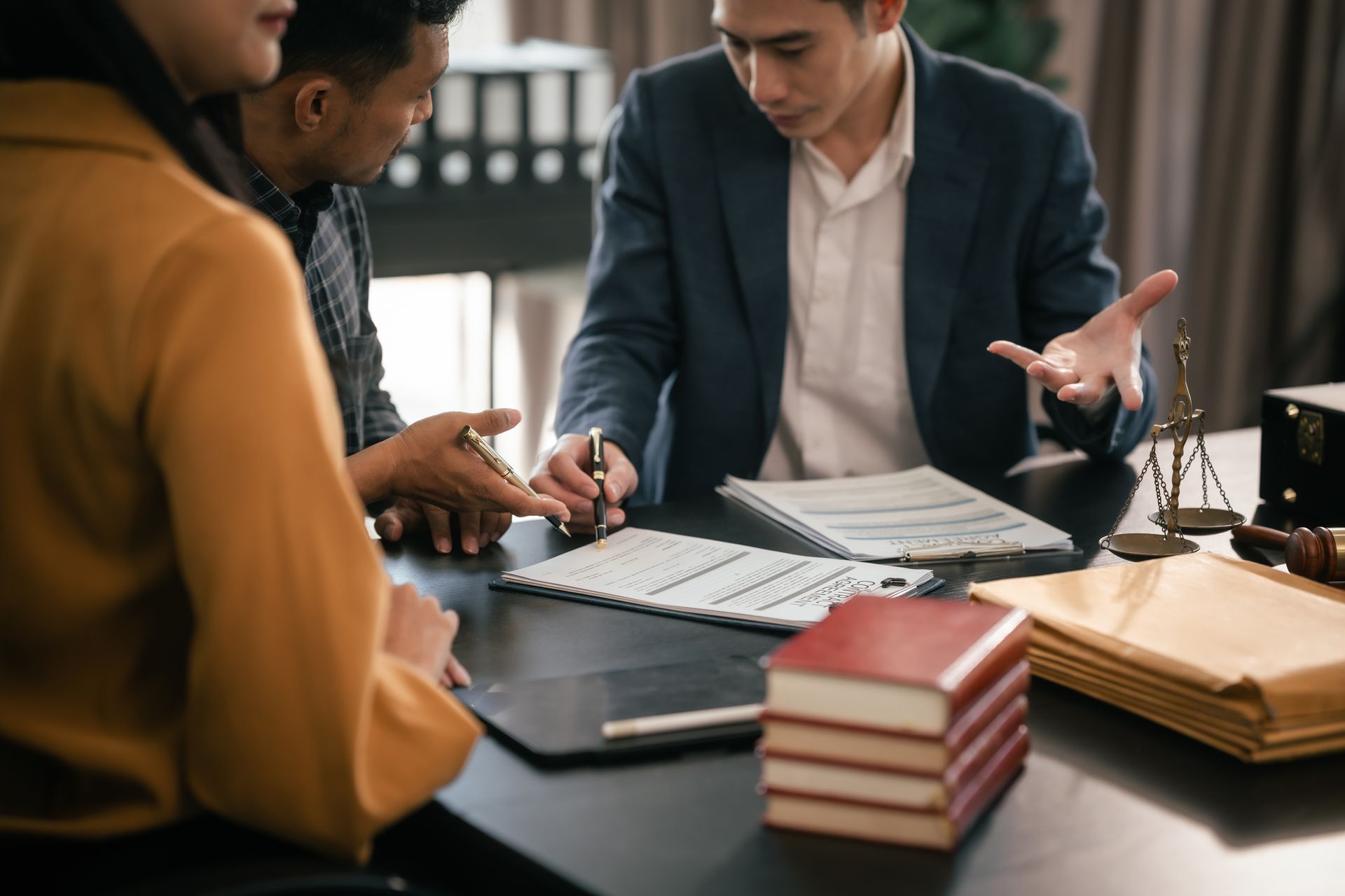 Group meeting around a desk with papers, laptop, keyboard, and stacked books.