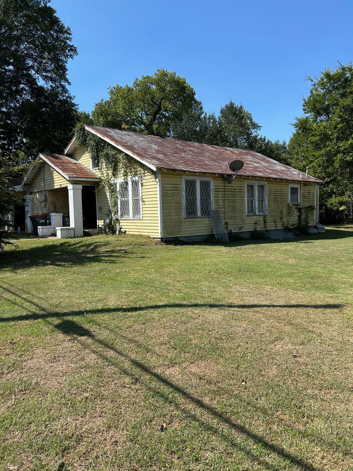 Old yellow house with red-tiled roof on a sunny grassy lawn, surrounded by trees