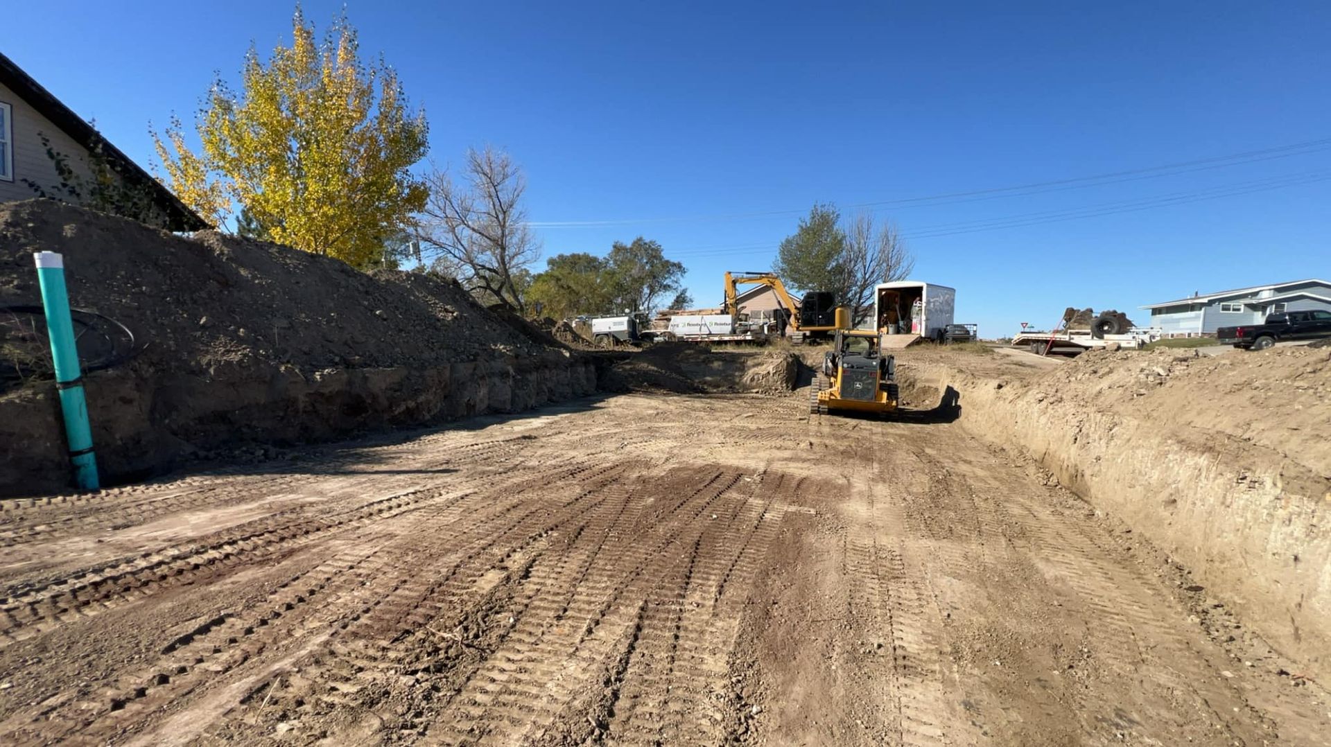 Construction site with a bulldozer, other equipment, and piles of dirt under a clear blue sky.