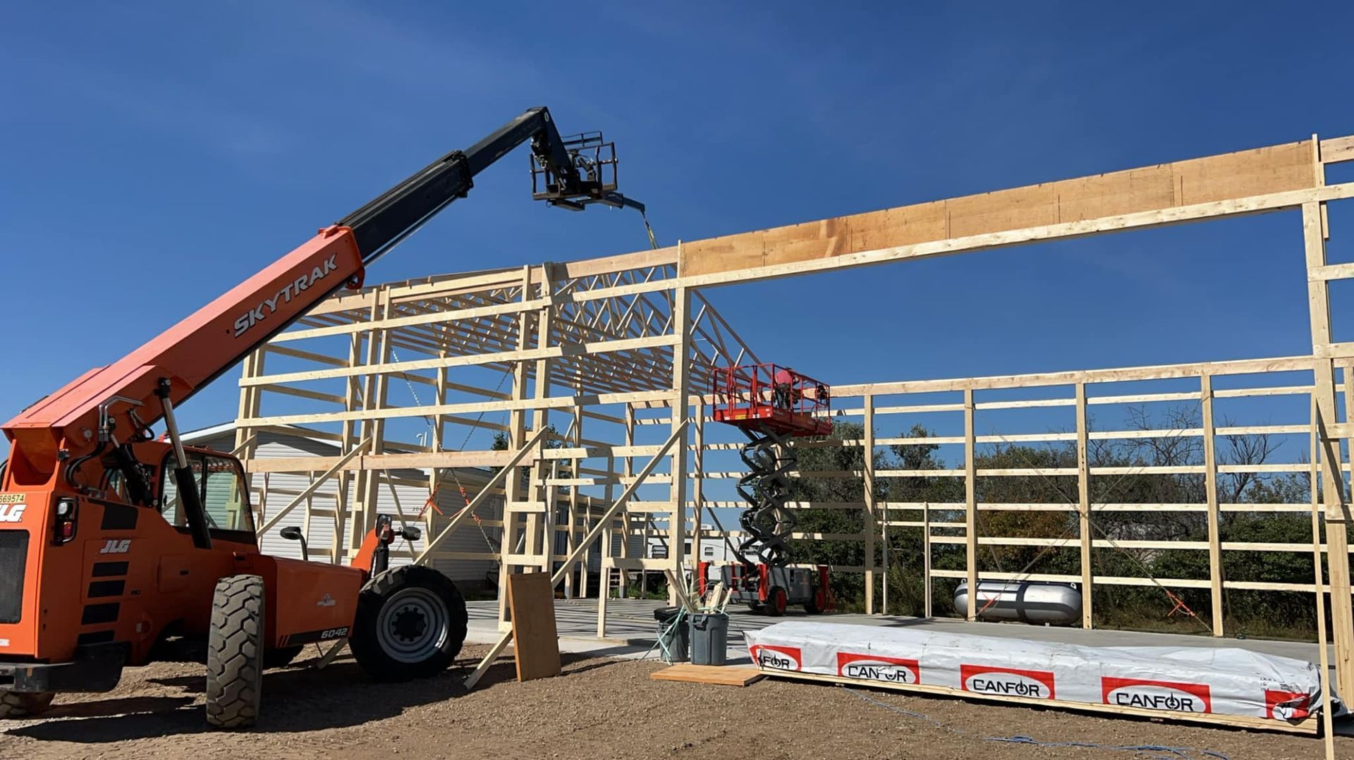 Construction of a wood-framed building; an orange forklift and a lift place beams under a blue sky.