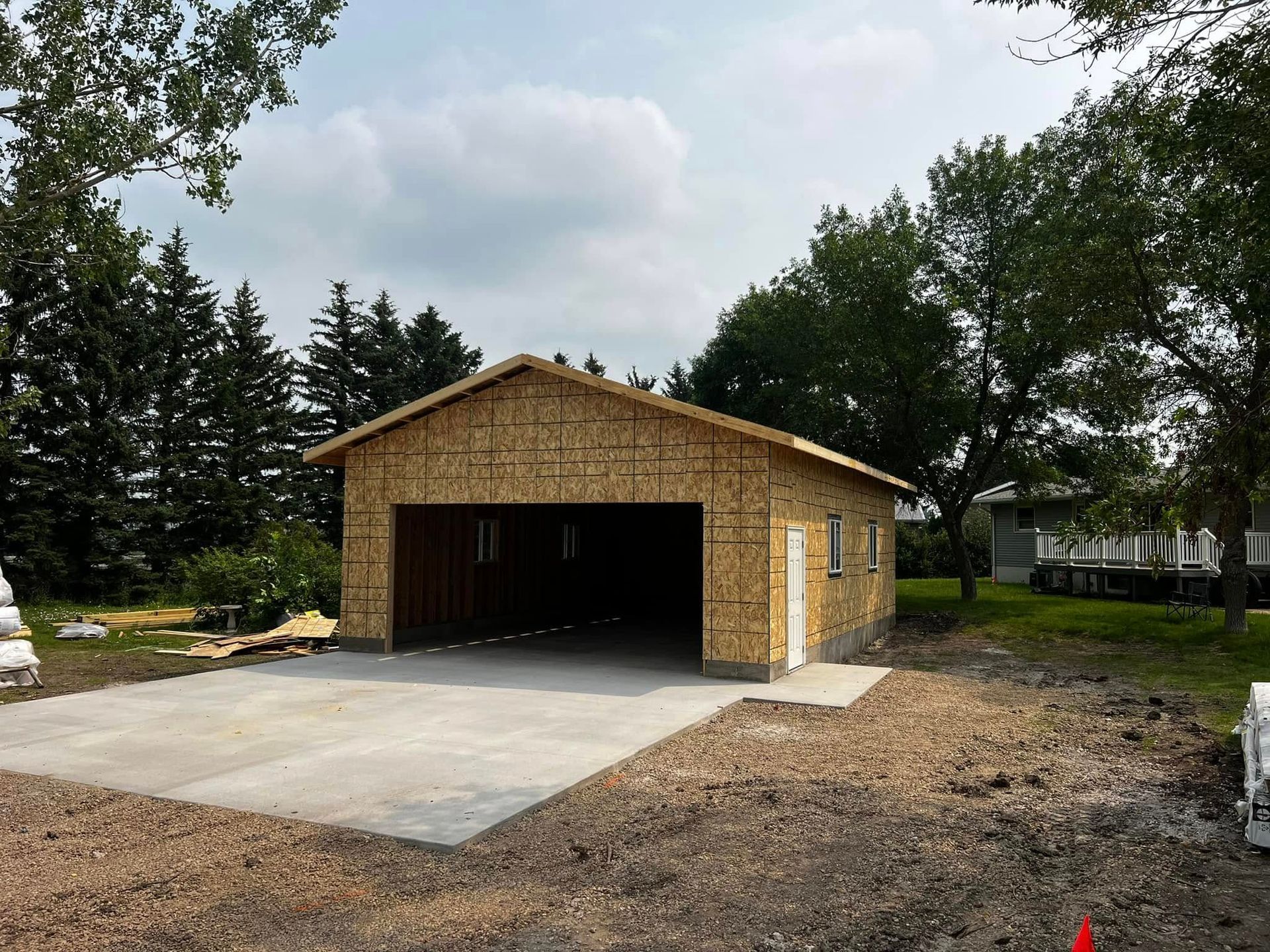 Garage under construction with concrete driveway, blue sky, and trees in background.