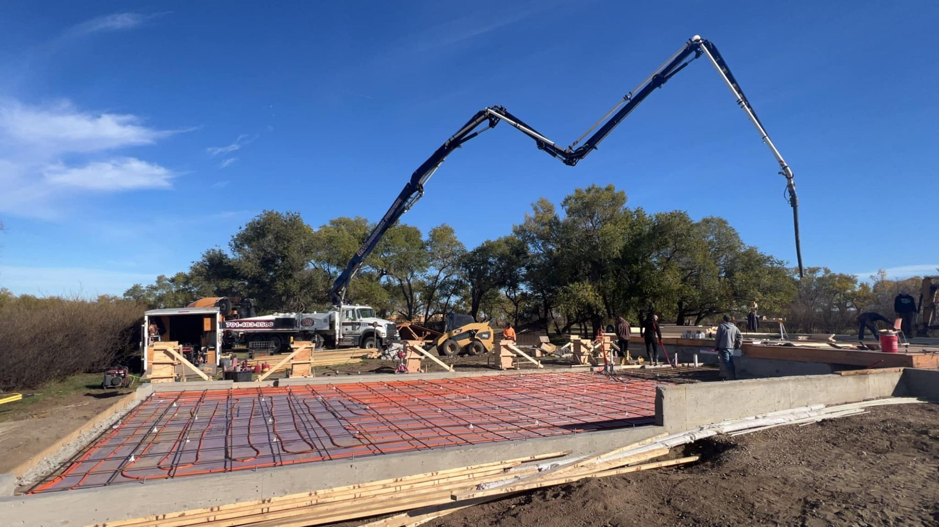 Concrete being poured on a construction site with a pump truck extending its arm, wooden forms, and workers.