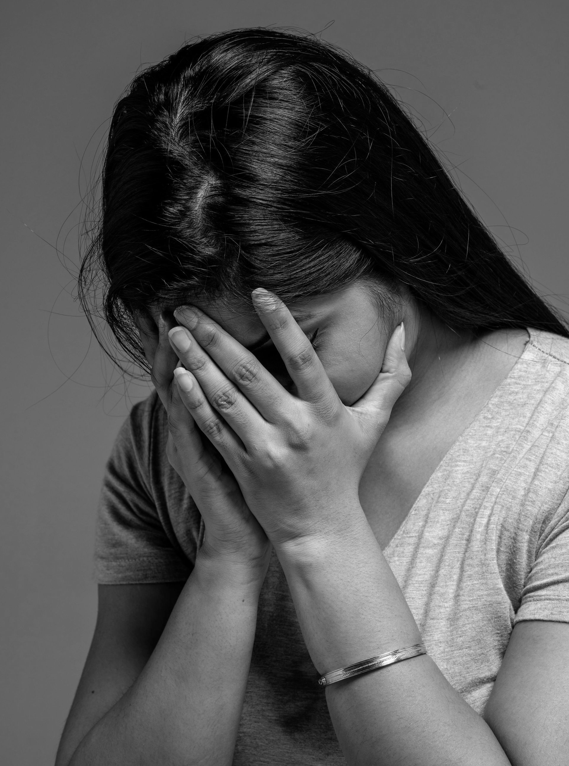 Woman with dark hair hides her face in her hands, appearing distressed.