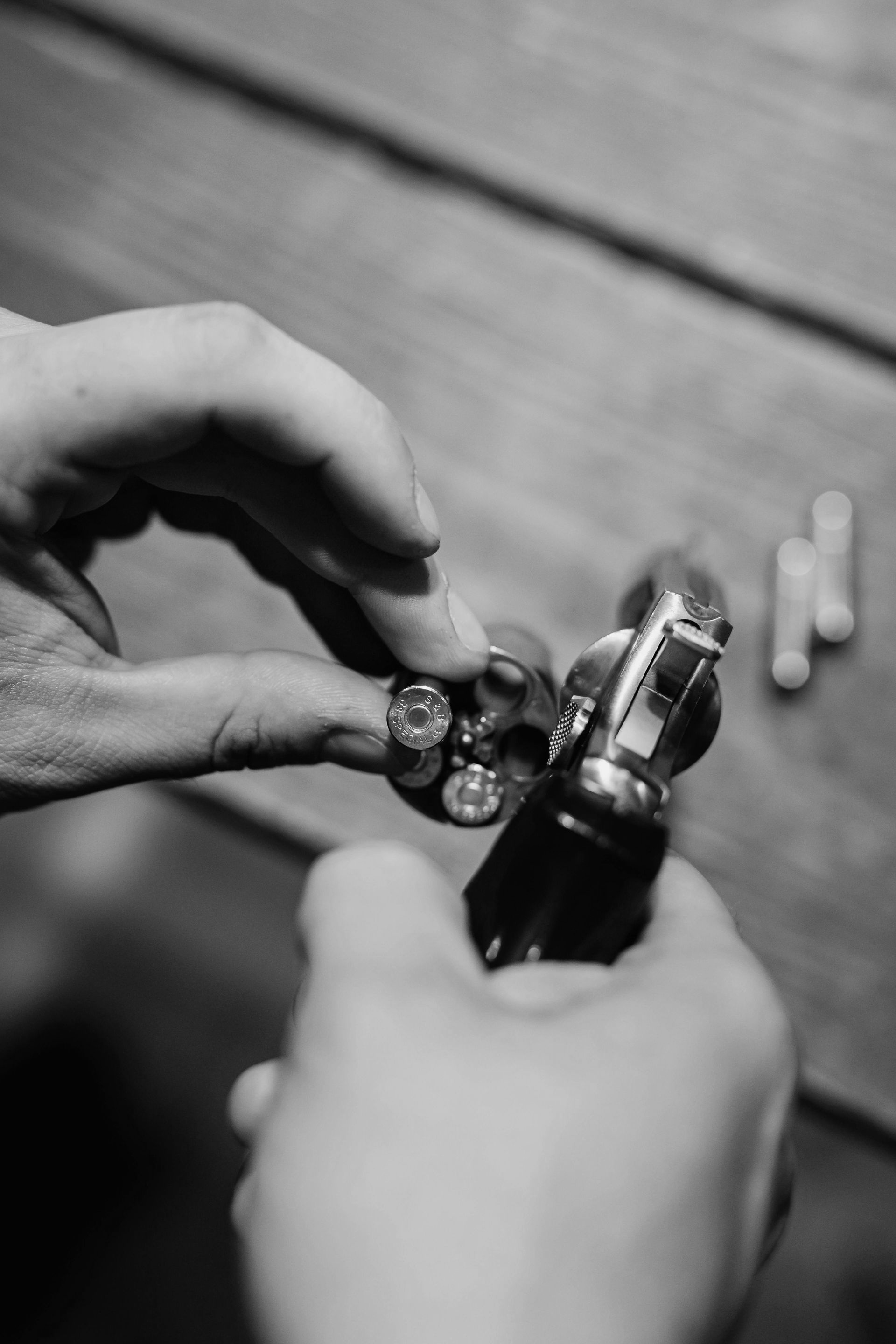 Hands loading ammunition into a revolver on a wooden surface.