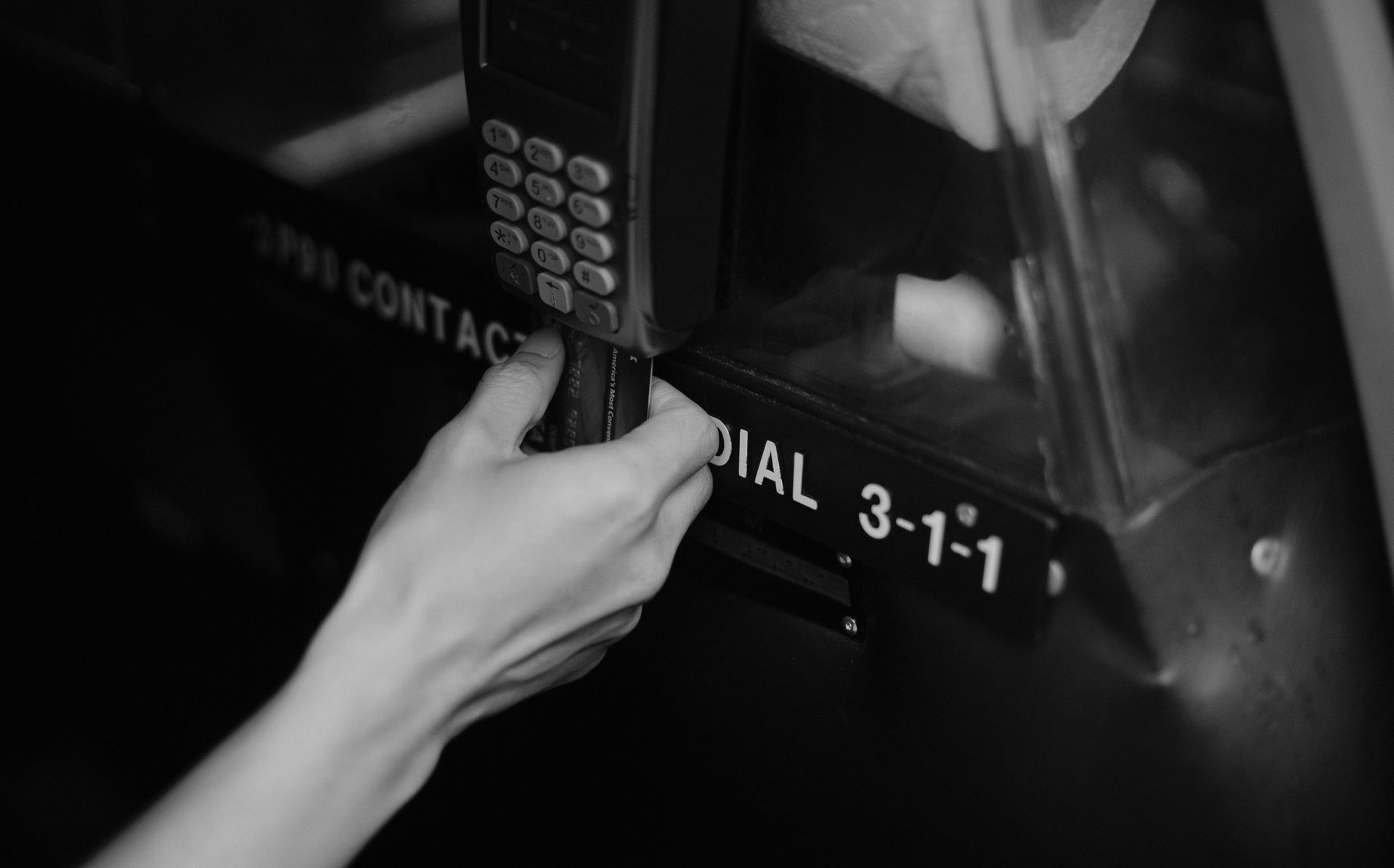 Hand reaching for a phone keypad on a payphone.