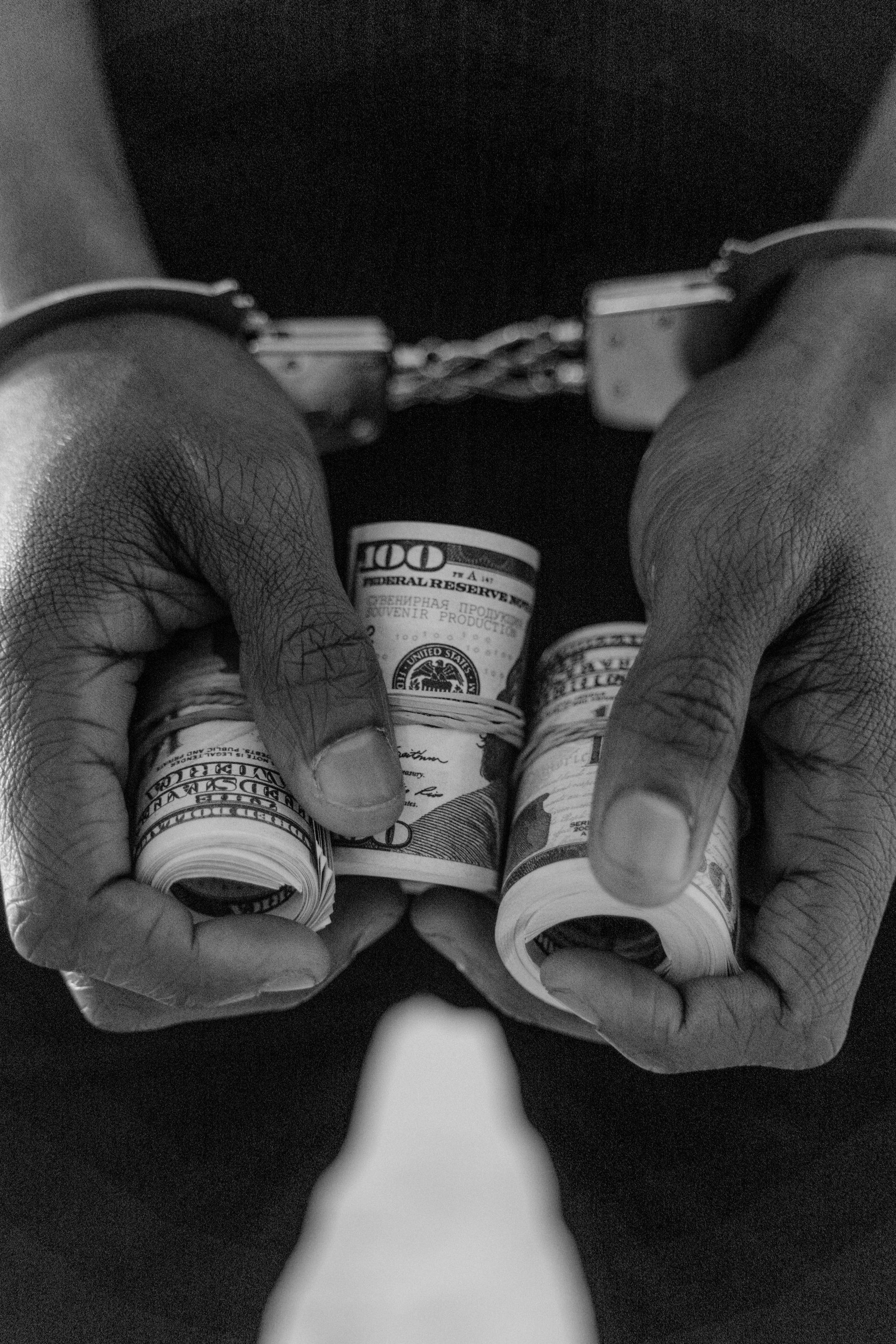 Person in handcuffs holding rolls of cash.