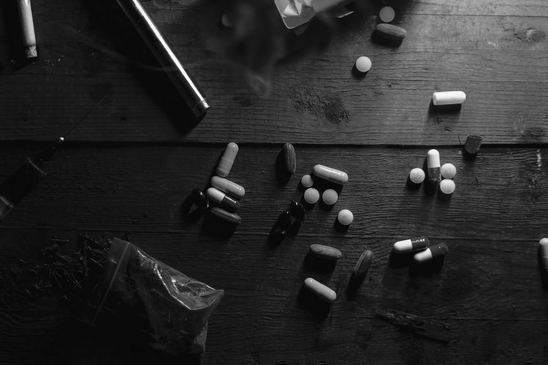 Pills and a metallic object lie on a dark wooden surface.