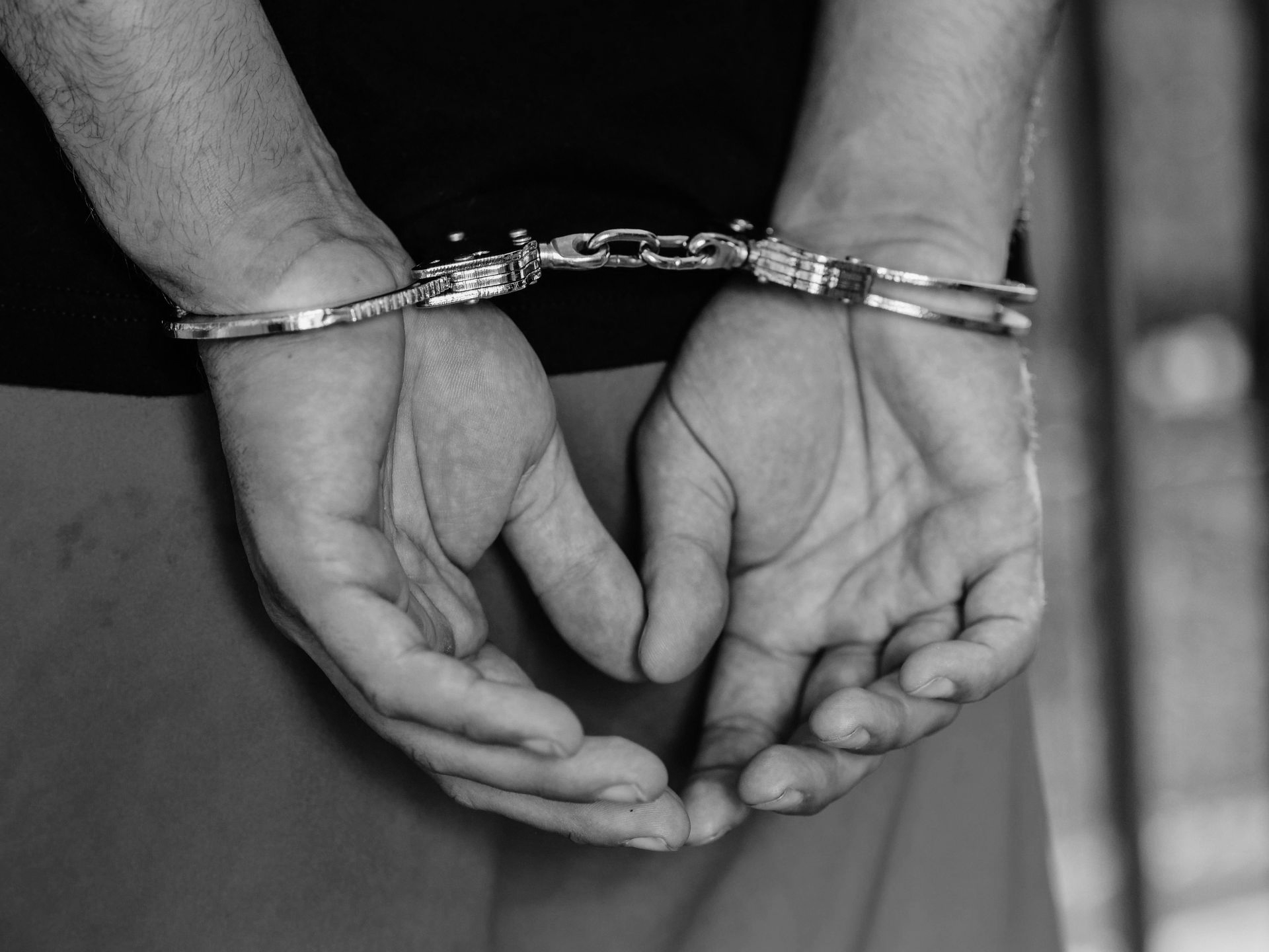 Hands clasped behind the back in handcuffs, person arrested.